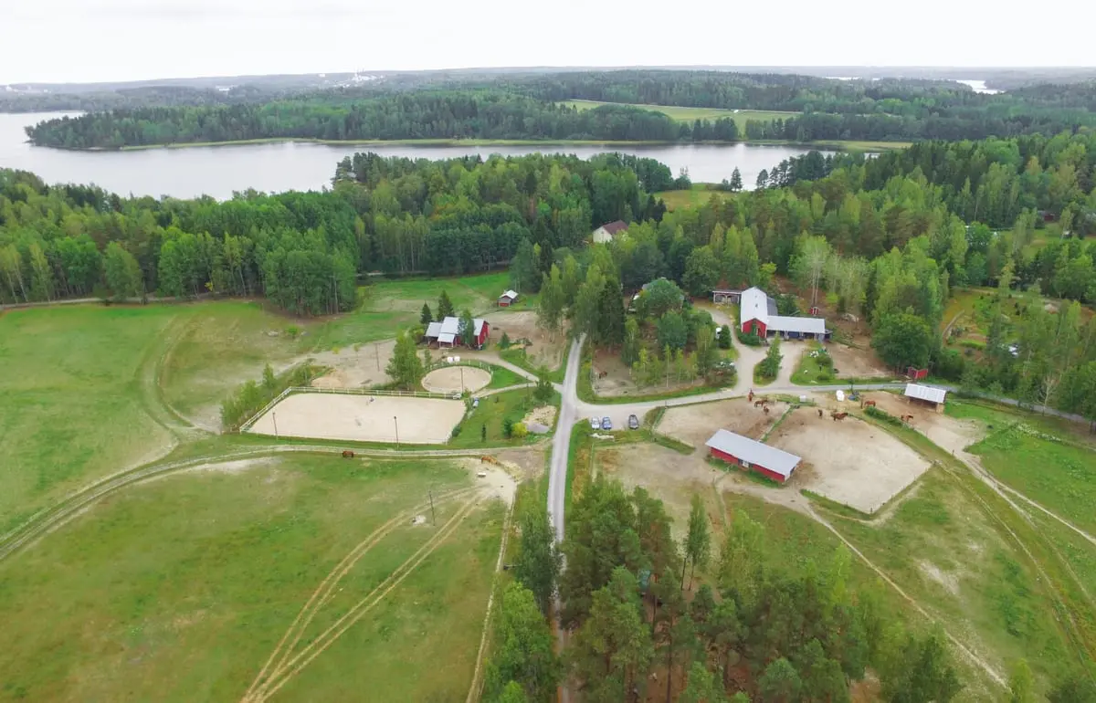 Ilmakuva hevostilasta laitumineen ja ratsastuskenttineen, järvi taustalla