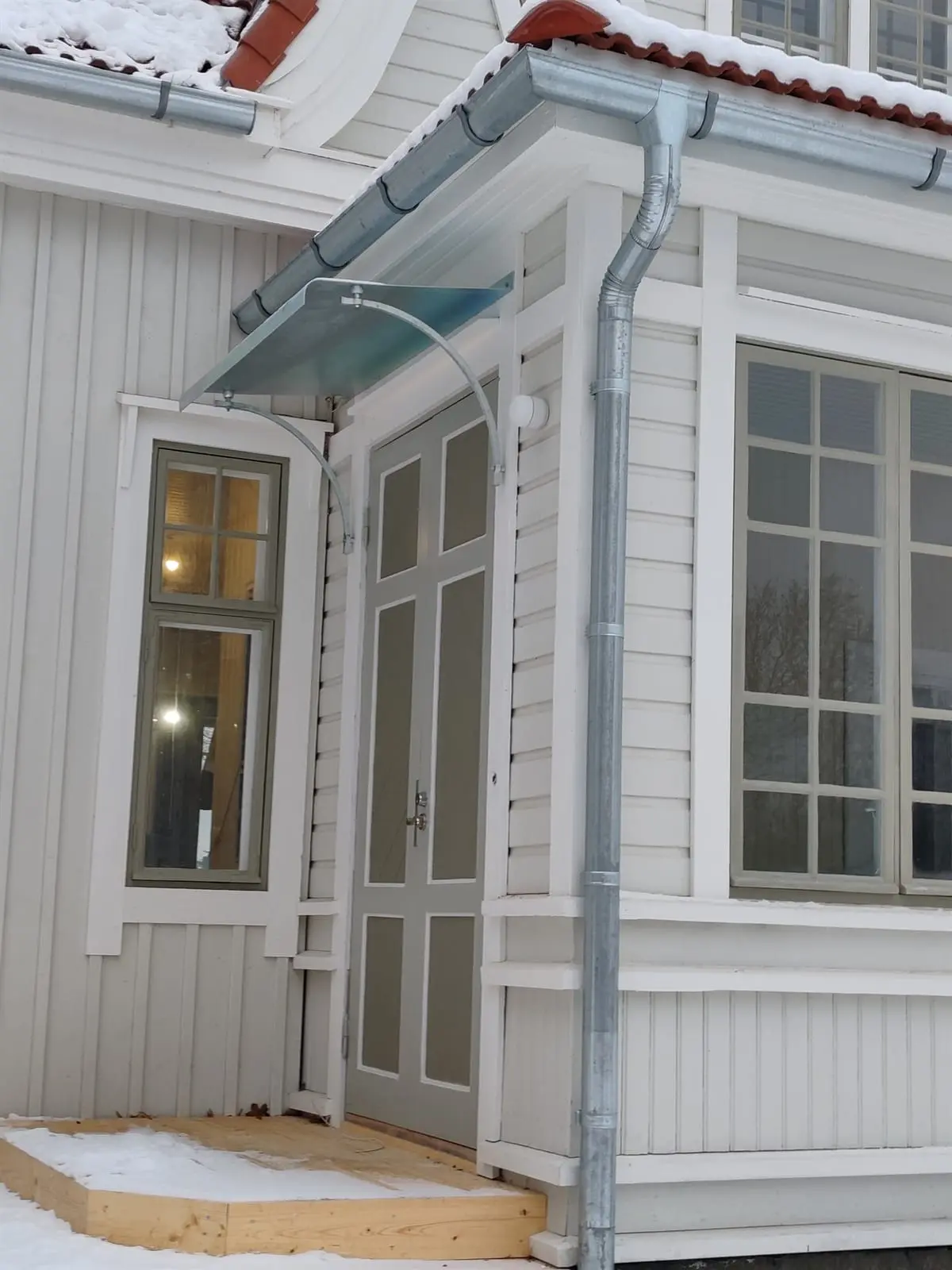 Sisäänkäynti talvella, lasinen katos oven yläpuolella