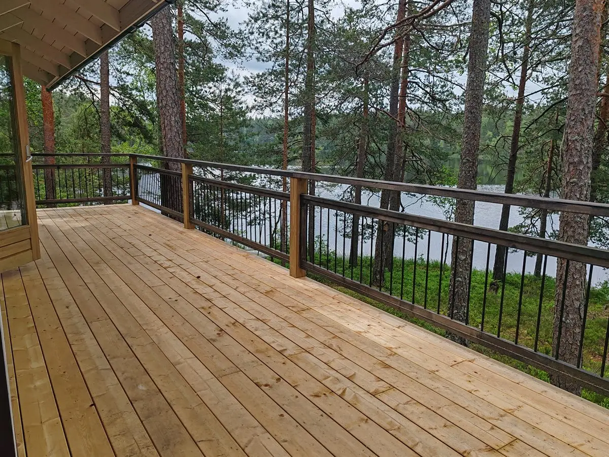 Uusi terassi mustine pinnakaiteineen, järvi männikön takana