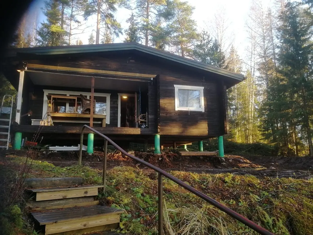 Mökki ennen peruskorjausta: tumma hirsirunko tuettuna pilareille