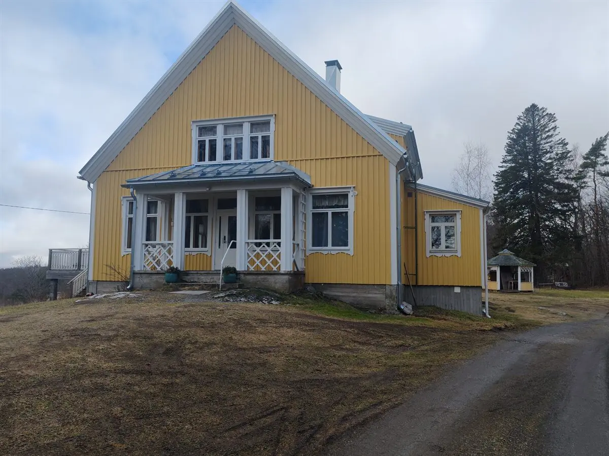 Keltainen puurakenteinen seurantalo mäellä, valkoinen lasikuisti ja ristikkokaiteet